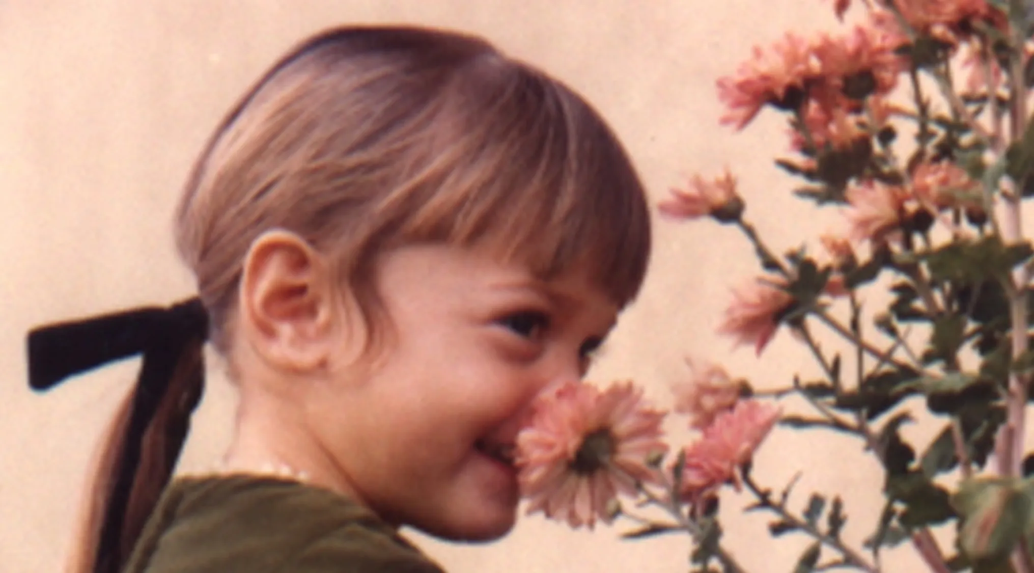 Young girl with a ponytail smiling and smelling pink flowers in a charming celebrities as kids photo.