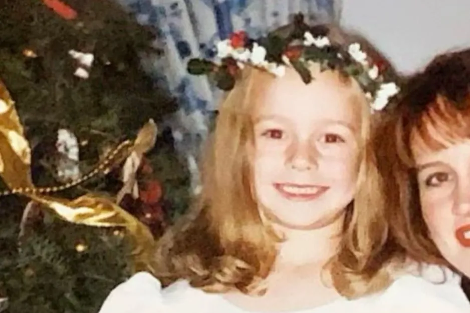 Young Brie Larson smiling, wearing a floral crown with a decorated Christmas tree in the background.
