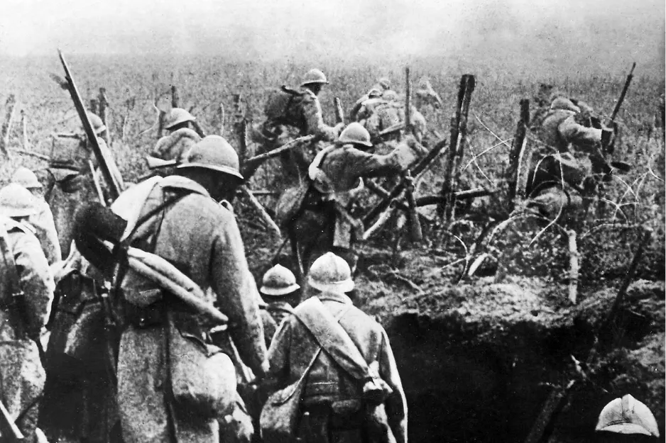 Soldiers advancing through barbed wire trenches during the start of World War I battle scene in black and white.