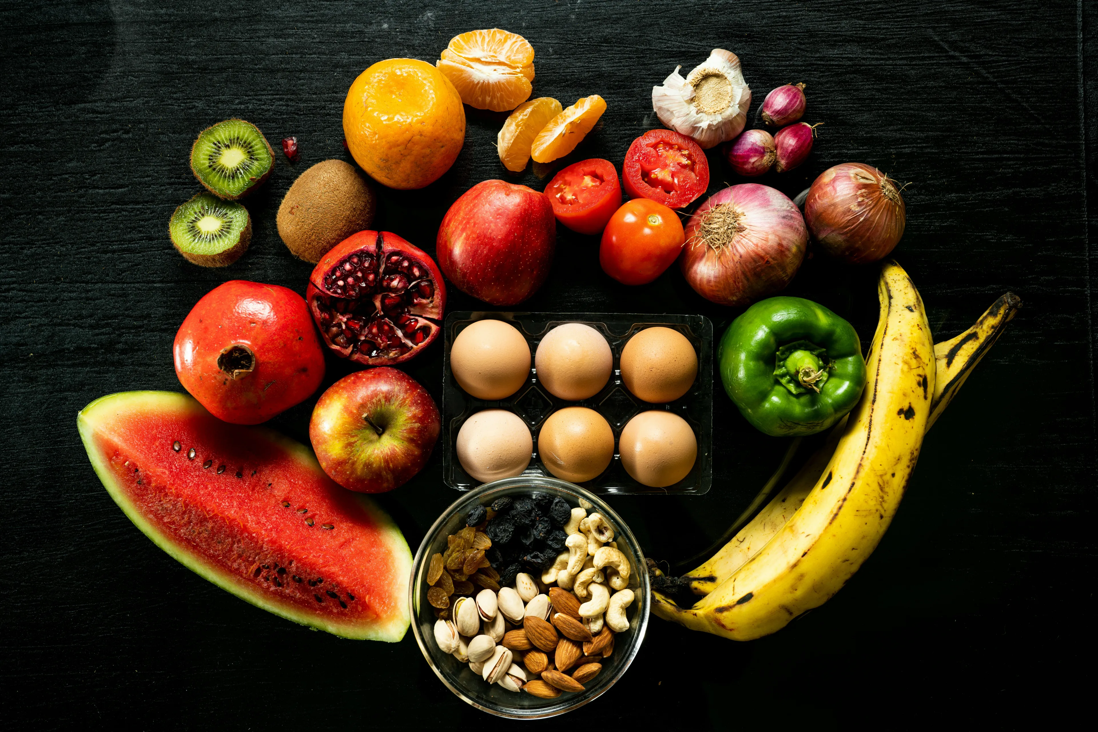 A variety of fruits, nuts, eggs, and vegetables displayed on a dark surface for nutrient absorption quiz concept.