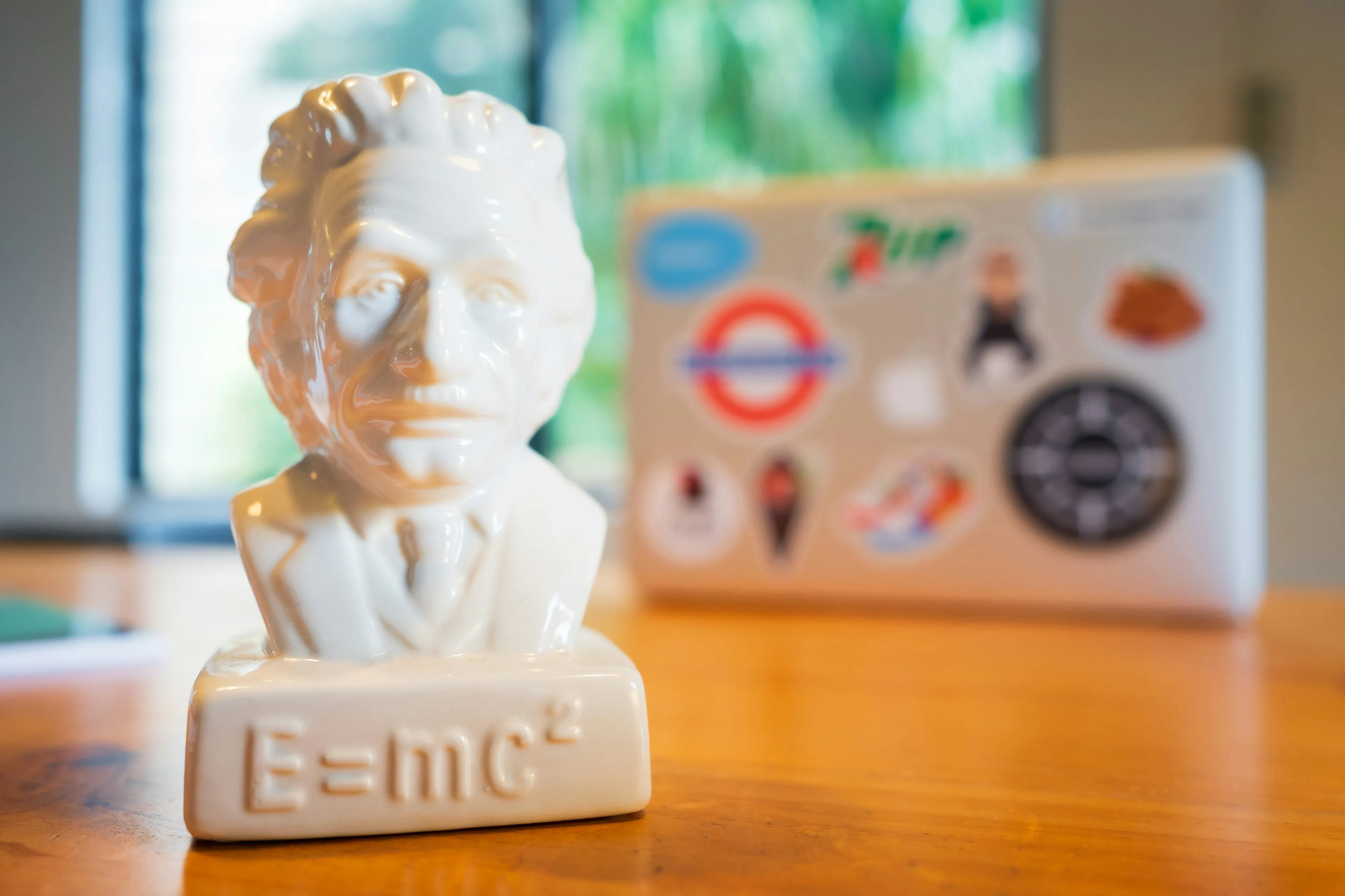 White ceramic bust of Einstein with E=mc squared engraved, placed on wooden table with blurred laptop in background, general knowledge quiz.