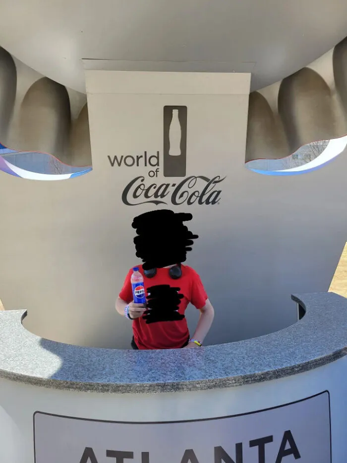 Un anarquista del primer mundo sostiene una Pepsi frente a un cartel de Coca-Cola, rompiendo las reglas por diversión.