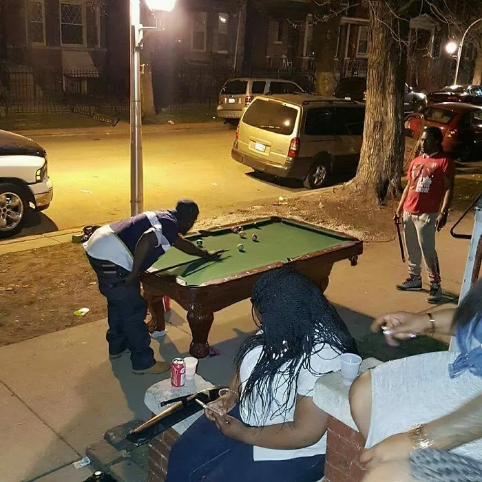 Personas jugando billar en la acera por la noche, reflejando la vida cotidiana en distintos estados de EEUU divertida y casual.