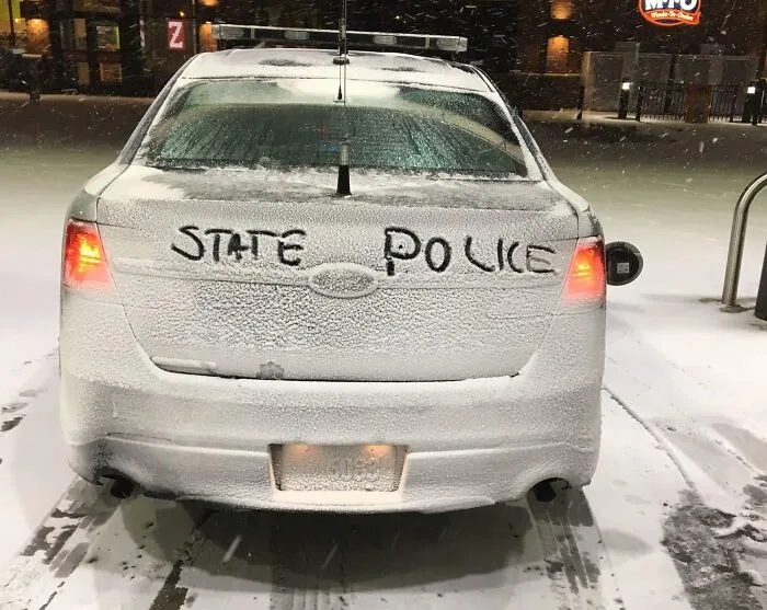 Coche de policía estatal cubierto de nieve con letras escritas en el cristal, representando la vida cotidiana en Estados Unidos.