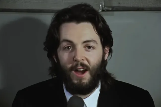 Man with beard and long hair speaking into a microphone, representing let it be by The Beatles on a road trip aux cord.