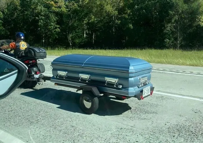 Motociclista remolcando un ataúd en carretera, imagen divertida que refleja la vida cotidiana en distintos estados de EEUU.