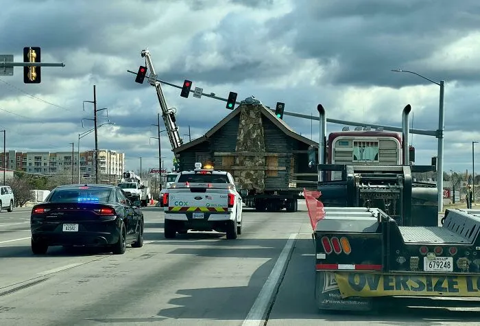 Casa antigua siendo trasladada en carretera, mostrando un momento cotidiano divertido en distintos estados de EEUU.