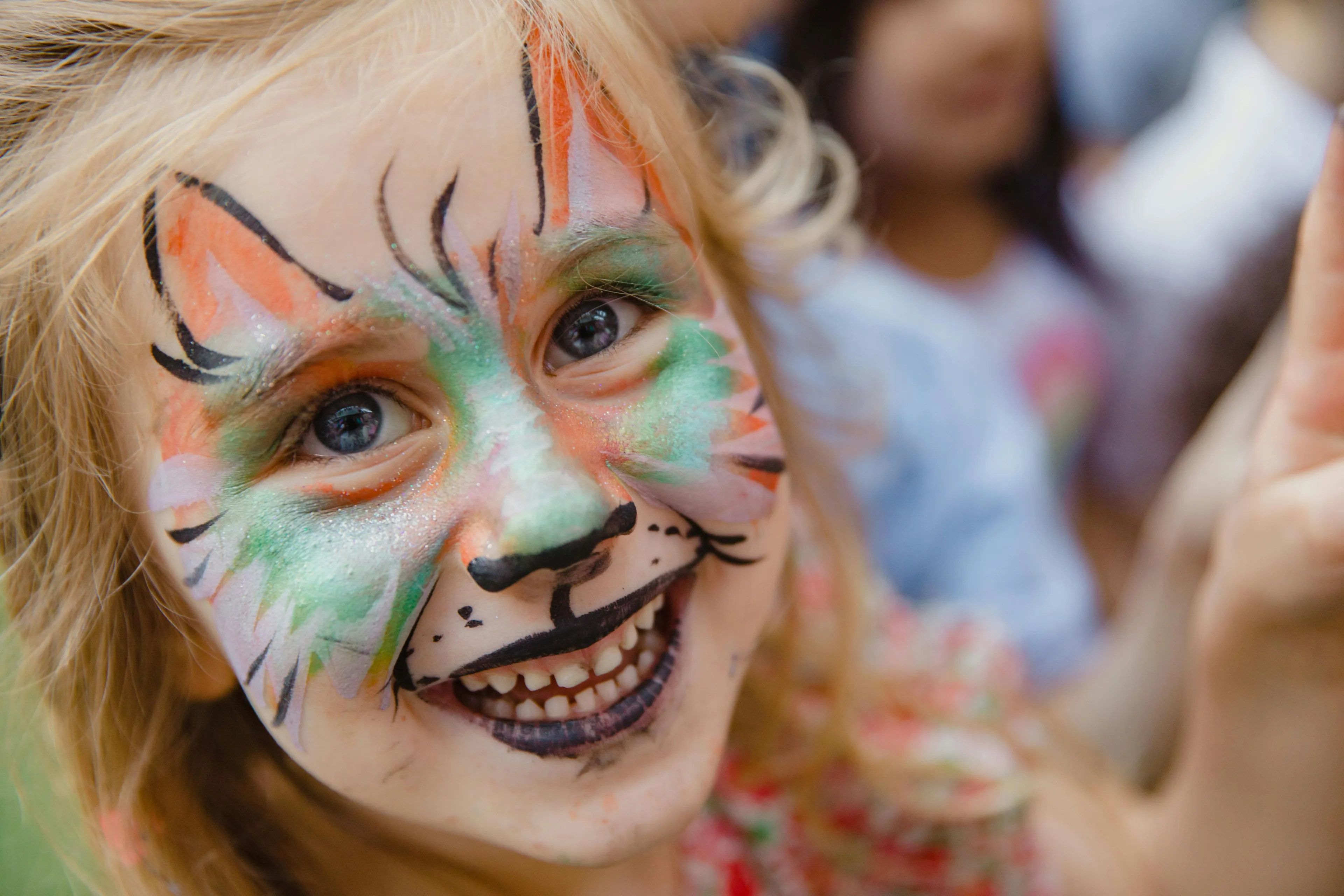 Young girl smiling with colorful face painting at a classic kid birthday party activity outdoors.