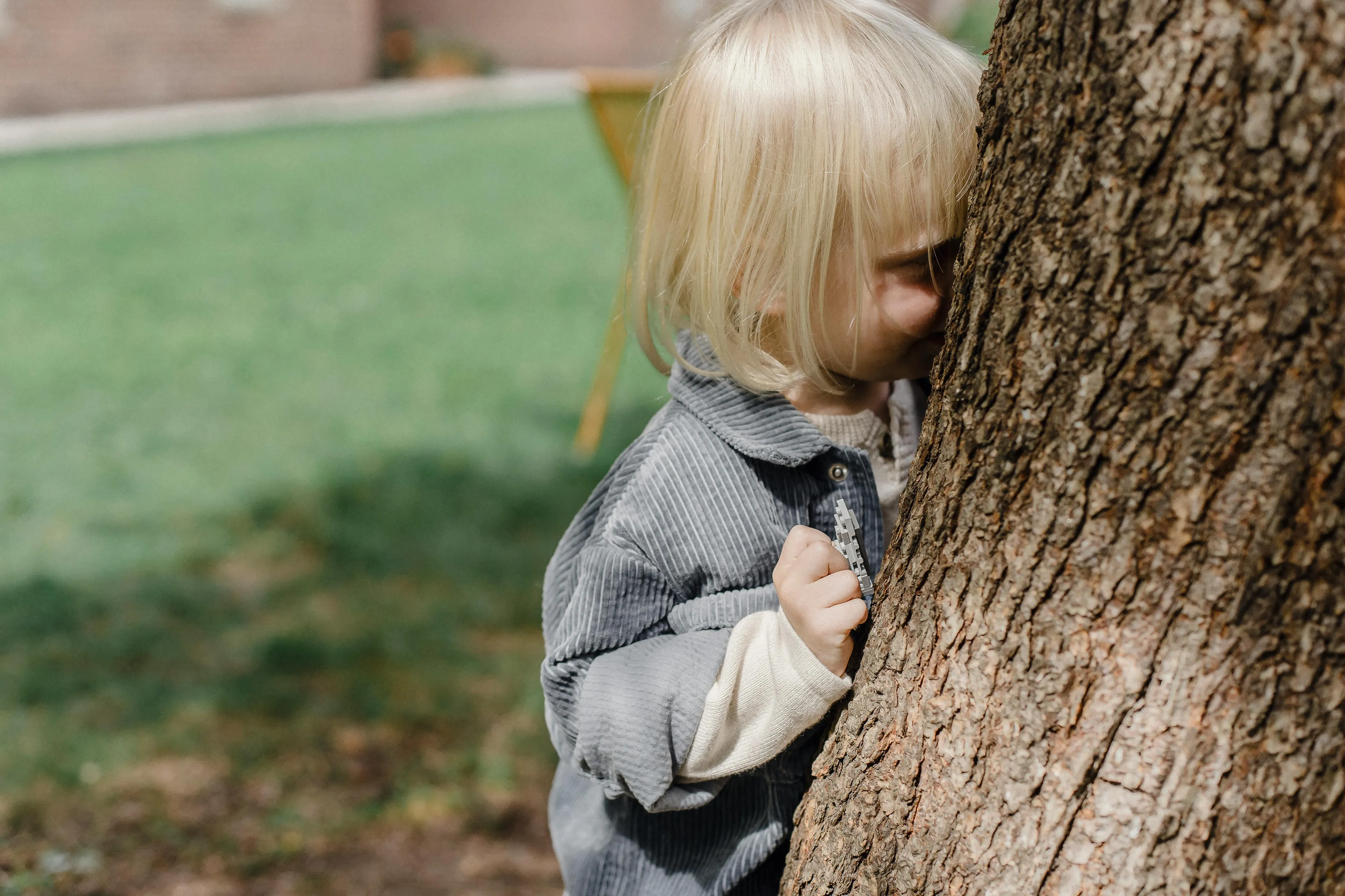 Young child playing hide-and-seek behind a tree outdoors, enjoying a classic kid birthday party activity.