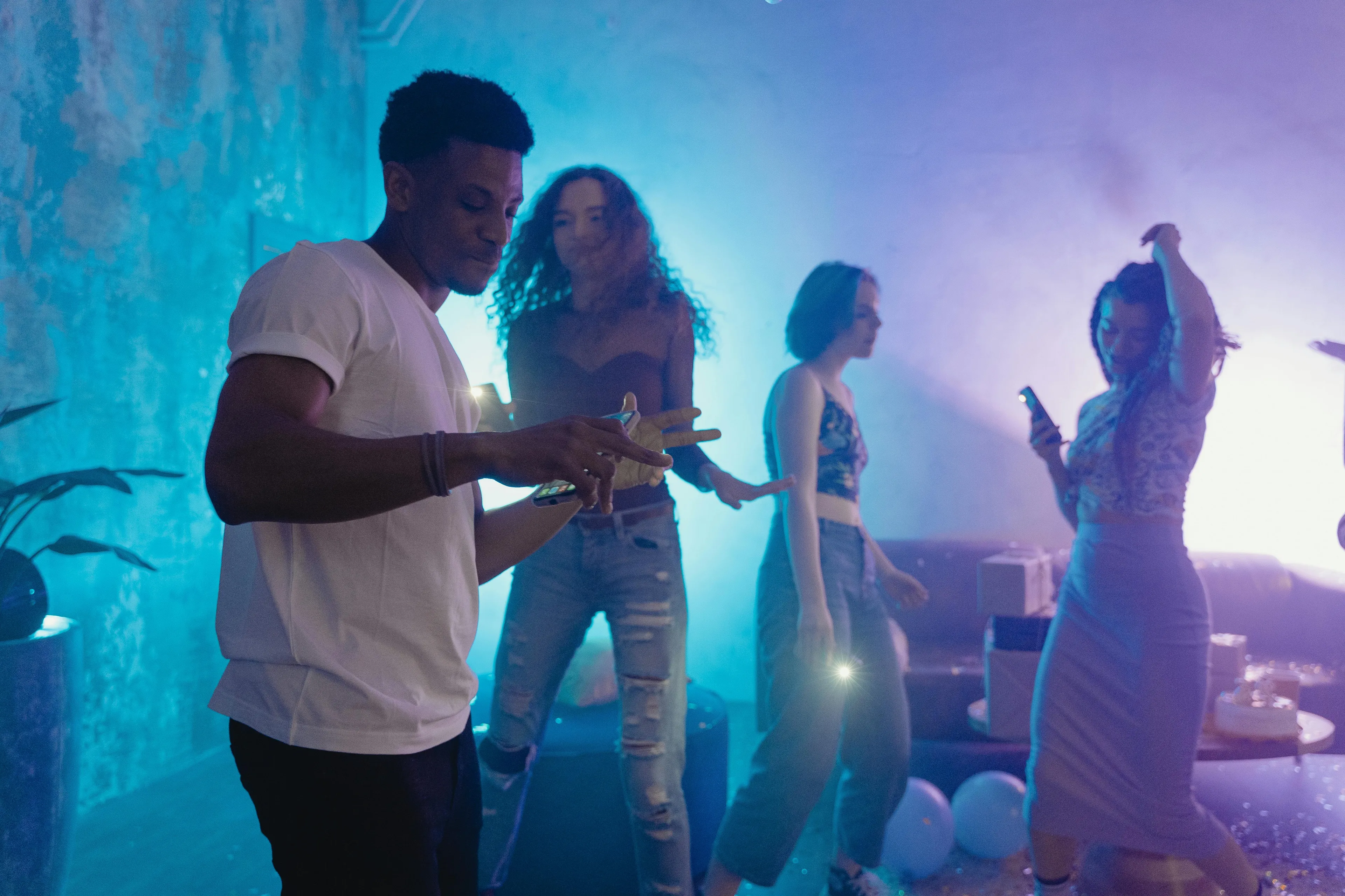 A group of young people dancing at a party with stalling playlist, unlocking inner group role vibe in dim colorful light.