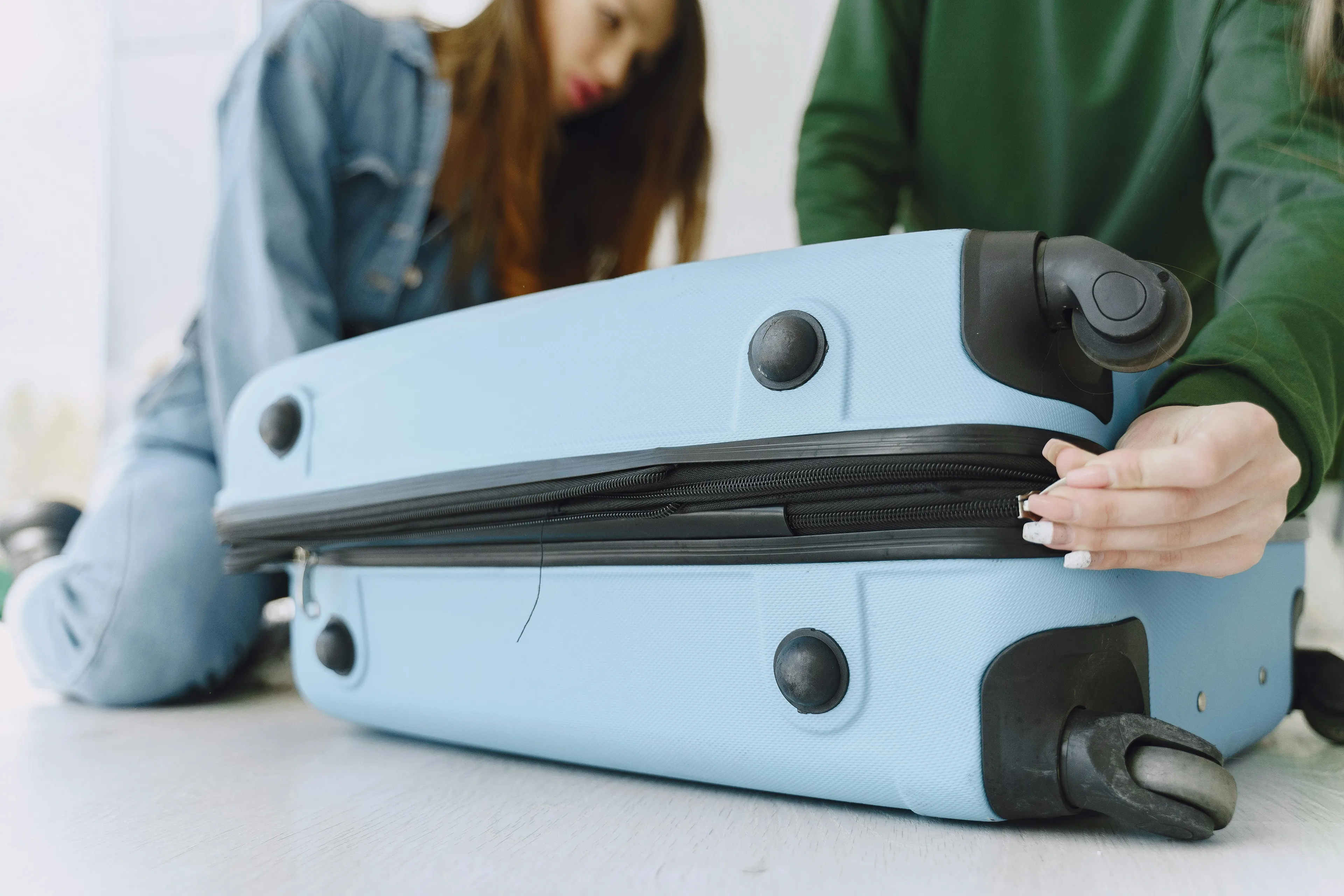 Two women interact with a light blue travel suitcase, exploring travel suitcase vibe and group role dynamics.