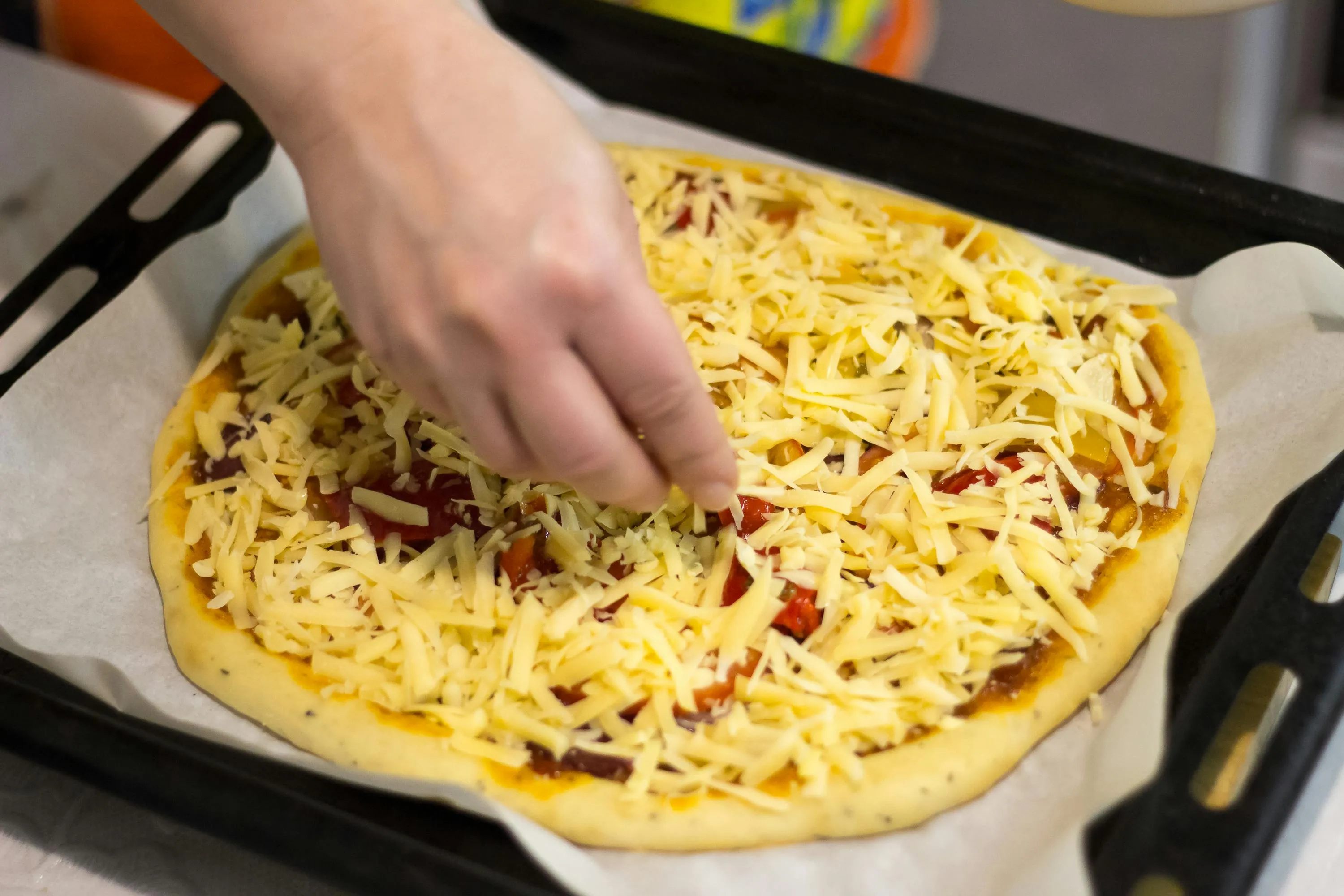 Hand placing toppings on a cheese-covered pizza, illustrating team group role in debating pizza preferences.