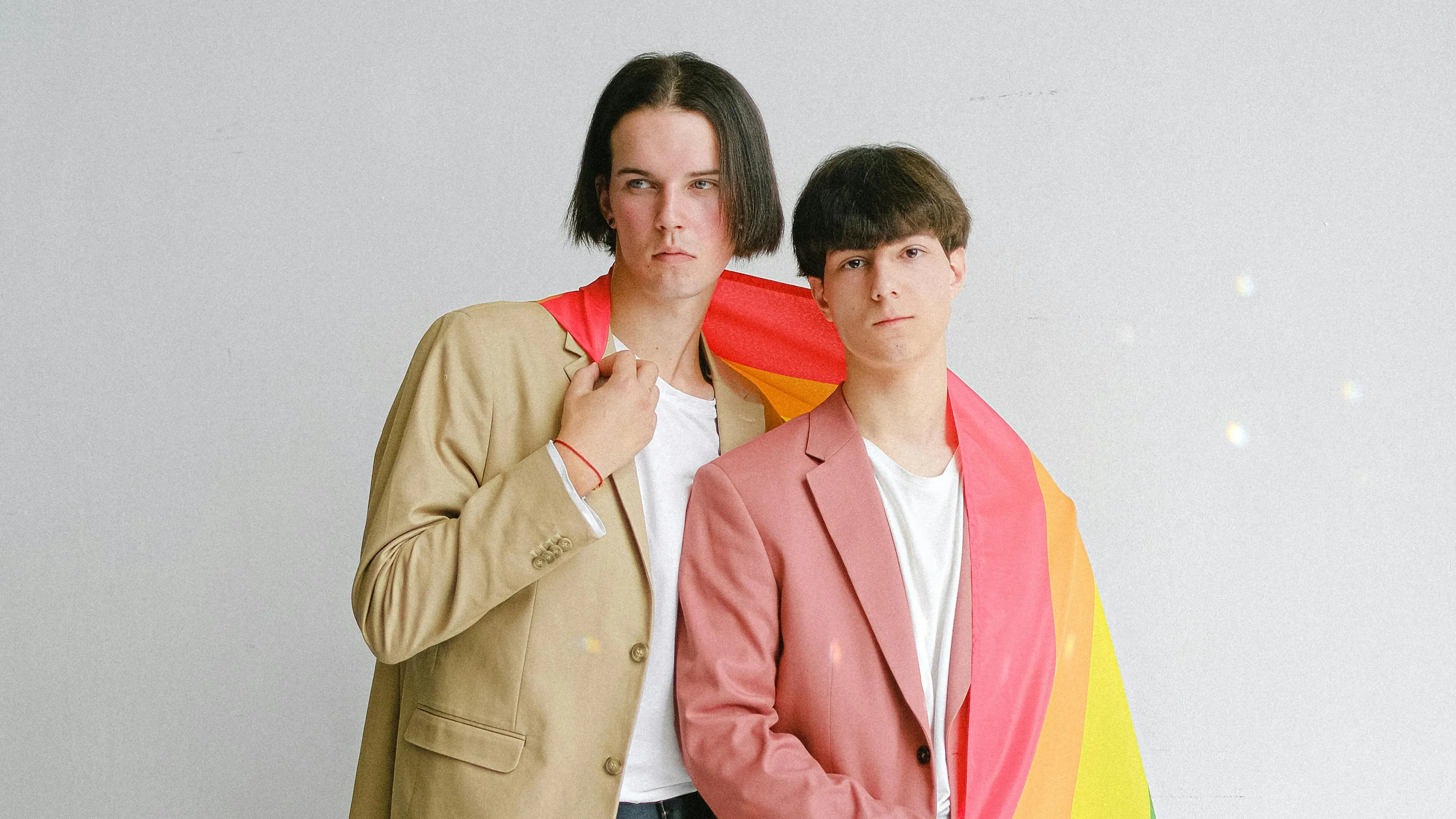 Two young men wearing blazers wrapped in a rainbow flag symbolizing countries that were first to legalize gay marriage.