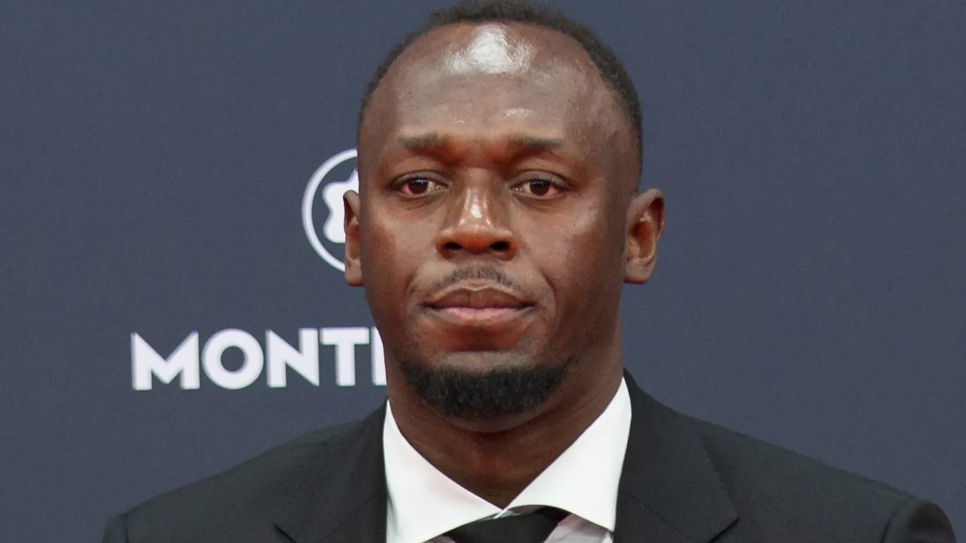 Usain Bolt in a black suit and white shirt at a press event, representing countries that were first in sprint records.