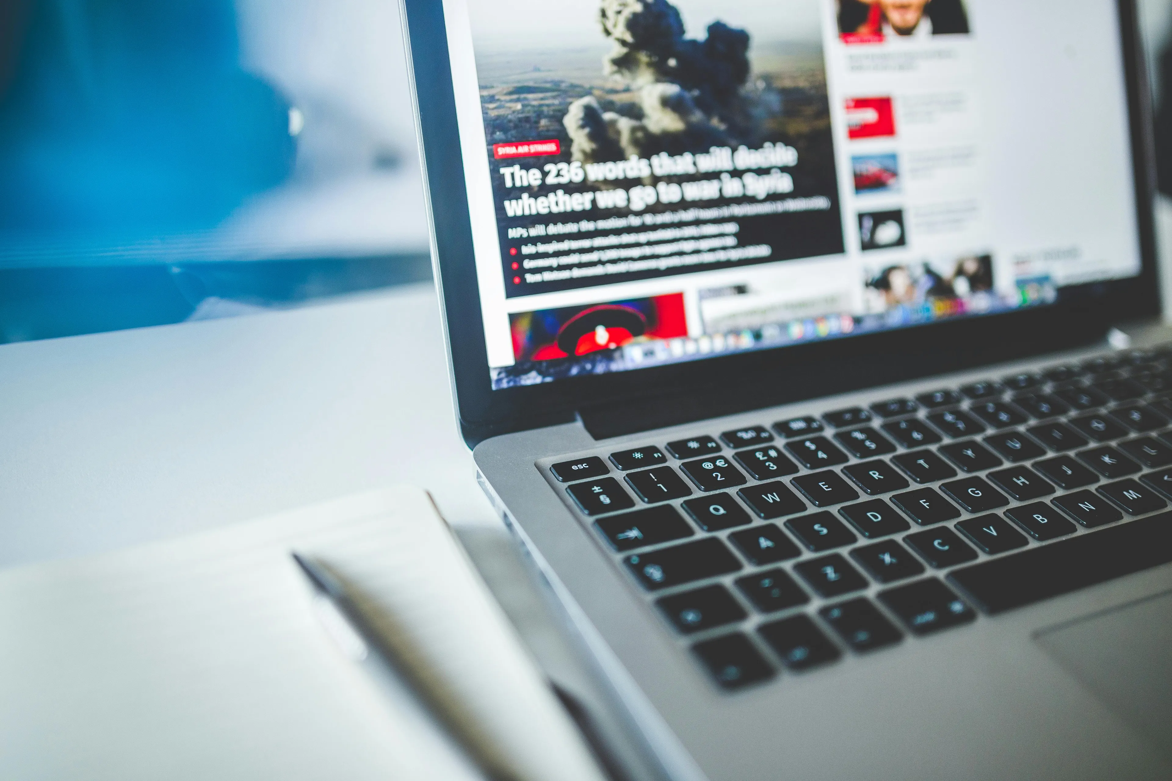 Laptop showing news website, illustrating internet access with a notebook and pen on a table in bright setting.