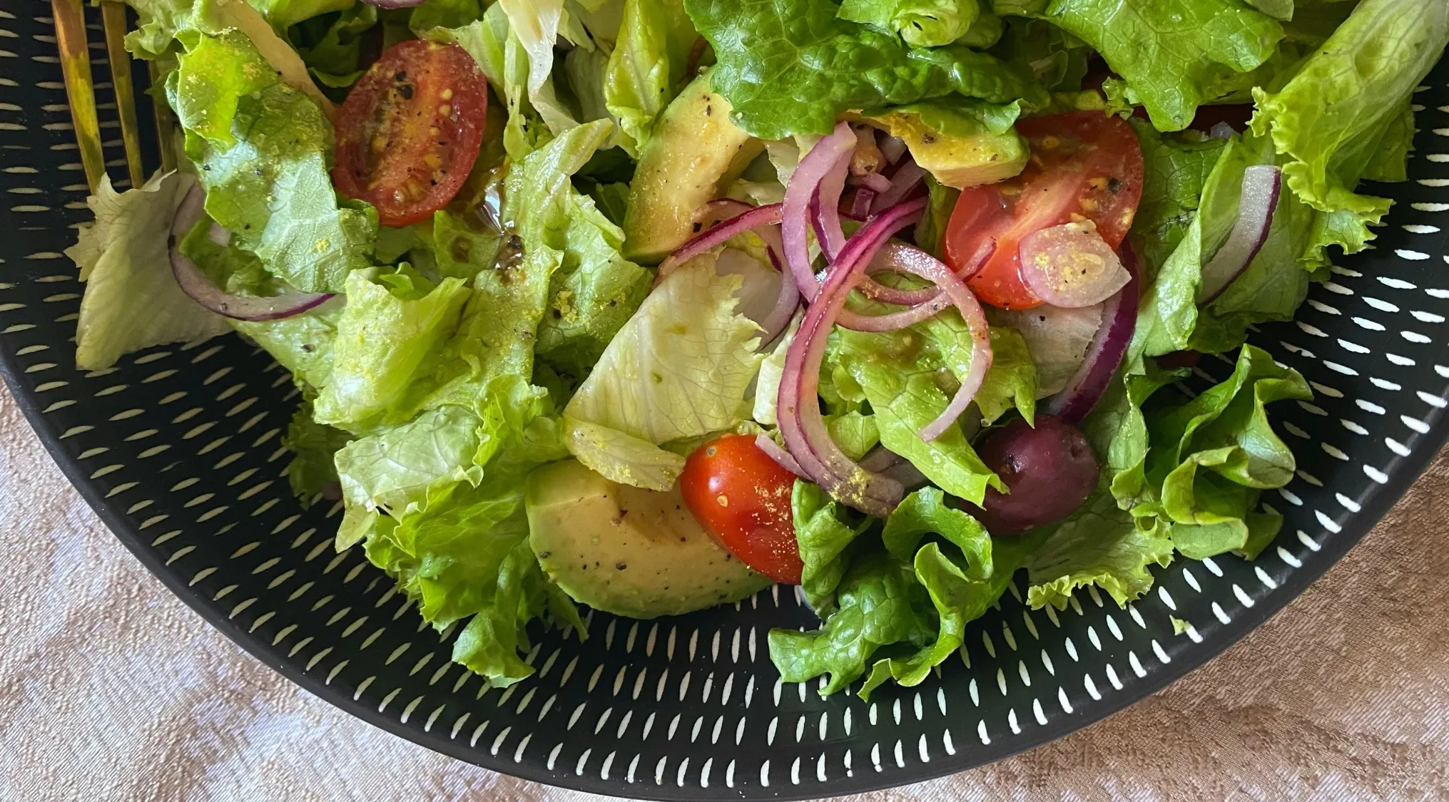 Fresh garden salad with lettuce, tomatoes, avocado, red onions, and olives in a black patterned bowl for two truths and a lie game