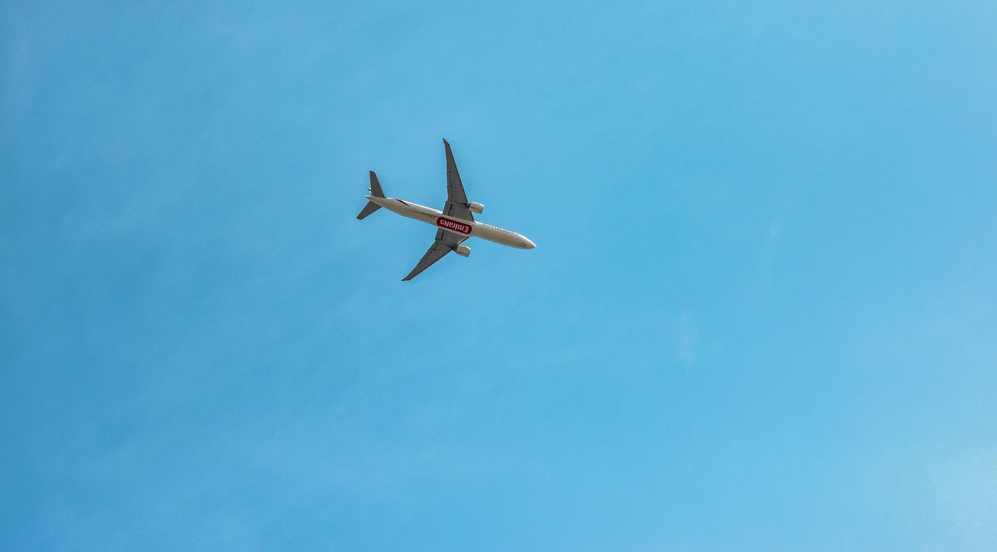 Commercial airplane flying in a clear blue sky, inviting viewers to play two truths and a lie game about travel.