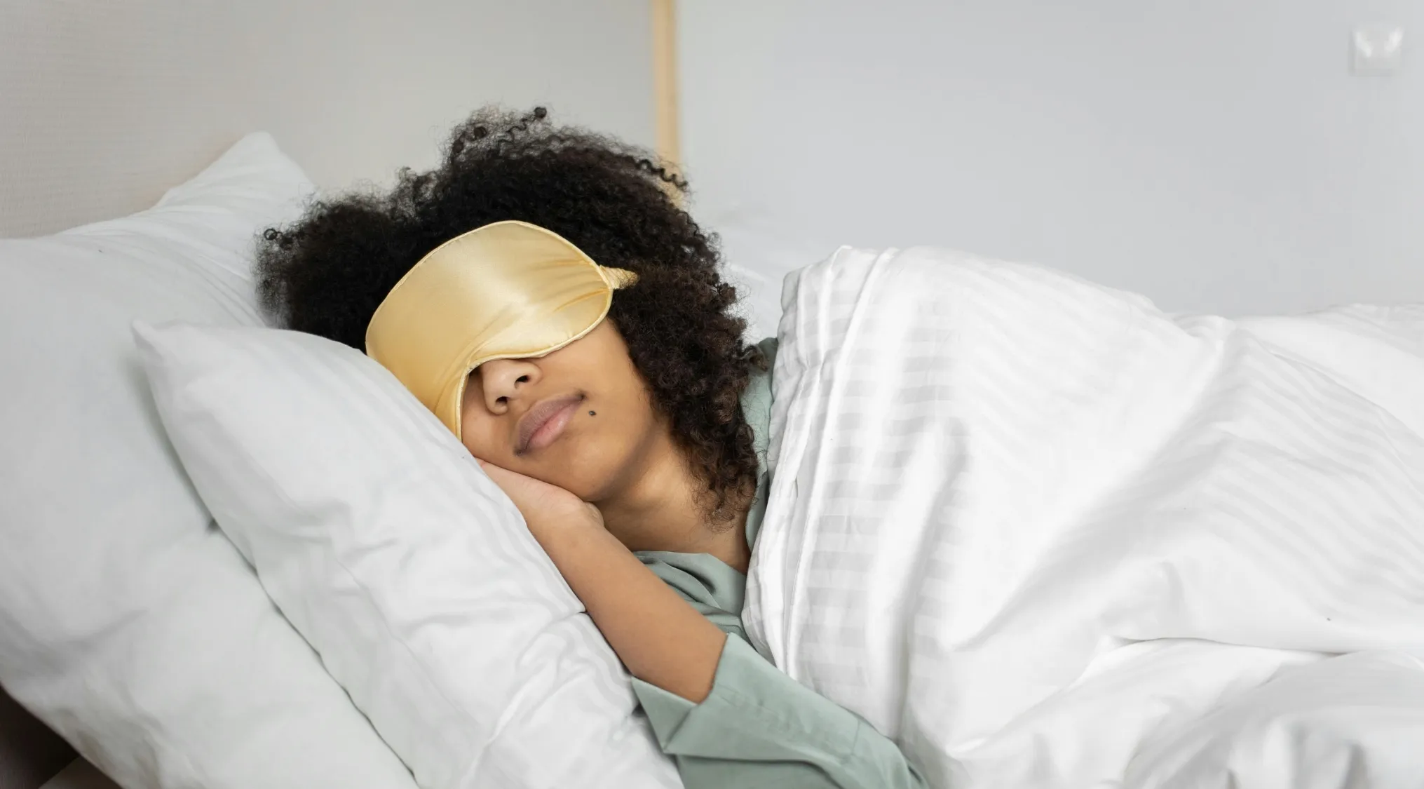 Person wearing a gold sleep mask resting on white pillows and blankets identifying the incorrect statement in two truths and a lie.
