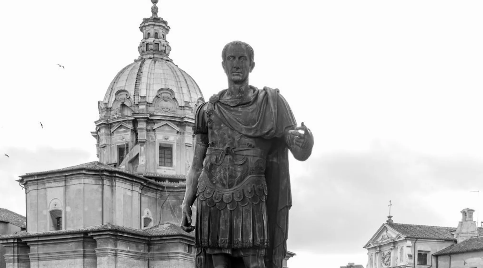 Statue of Julius Caesar in Roman armor with historic dome and buildings in the background representing the Roman Empire.