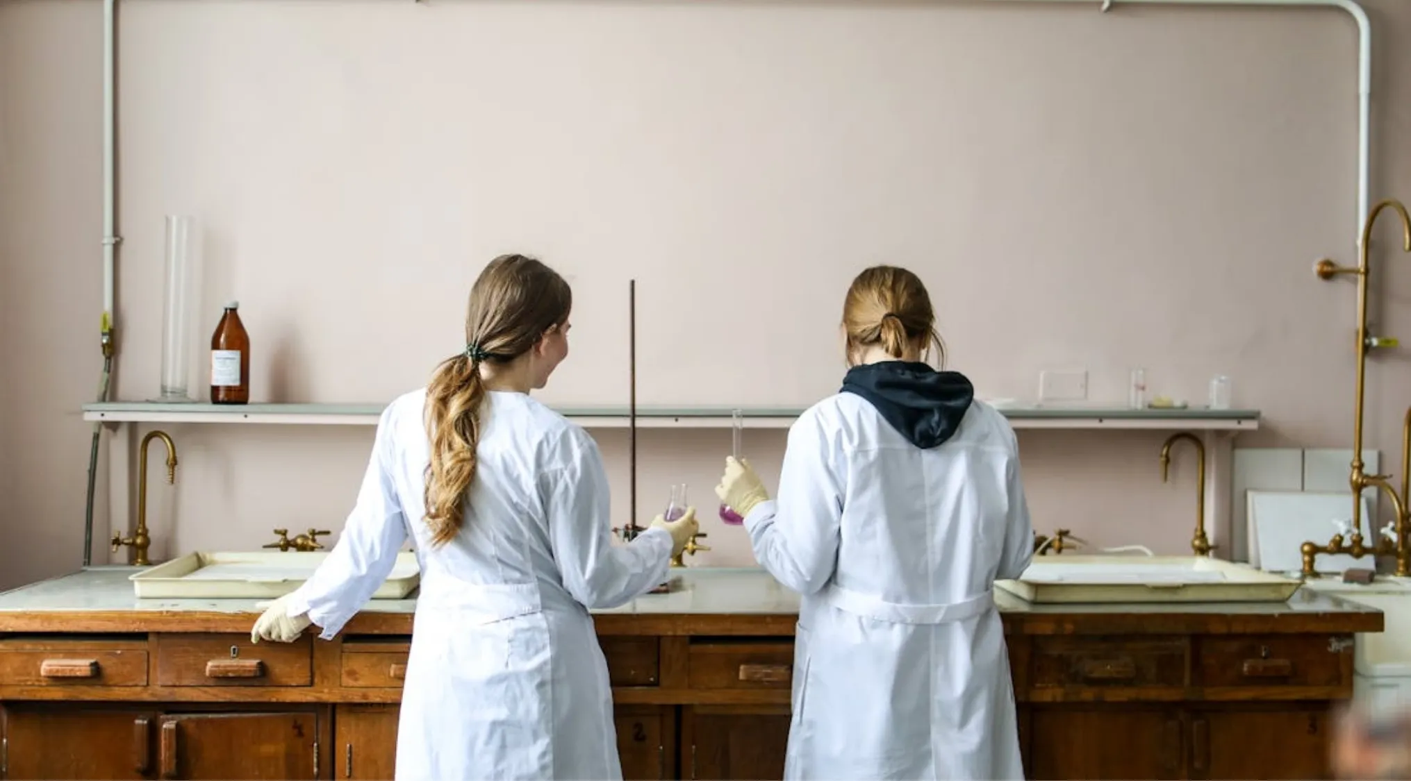 Two scientists in white lab coats holding test tubes in a chemistry lab with vintage wooden workbenches equipment