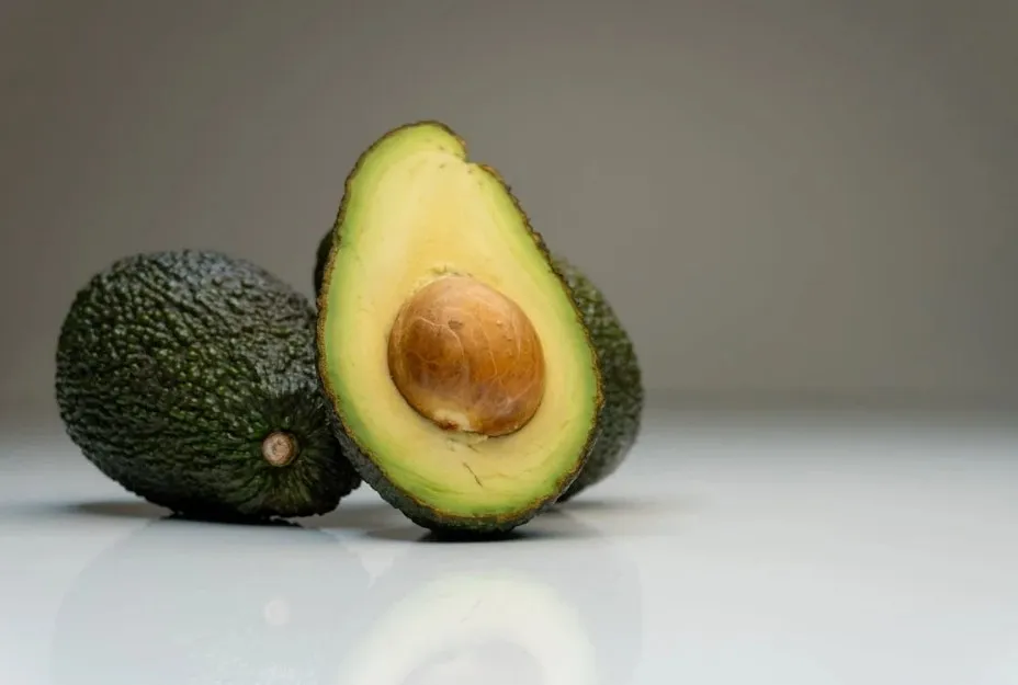 Two whole avocados and one avocado half showing the seed, illustrating avocado as a botanically classified fruit.