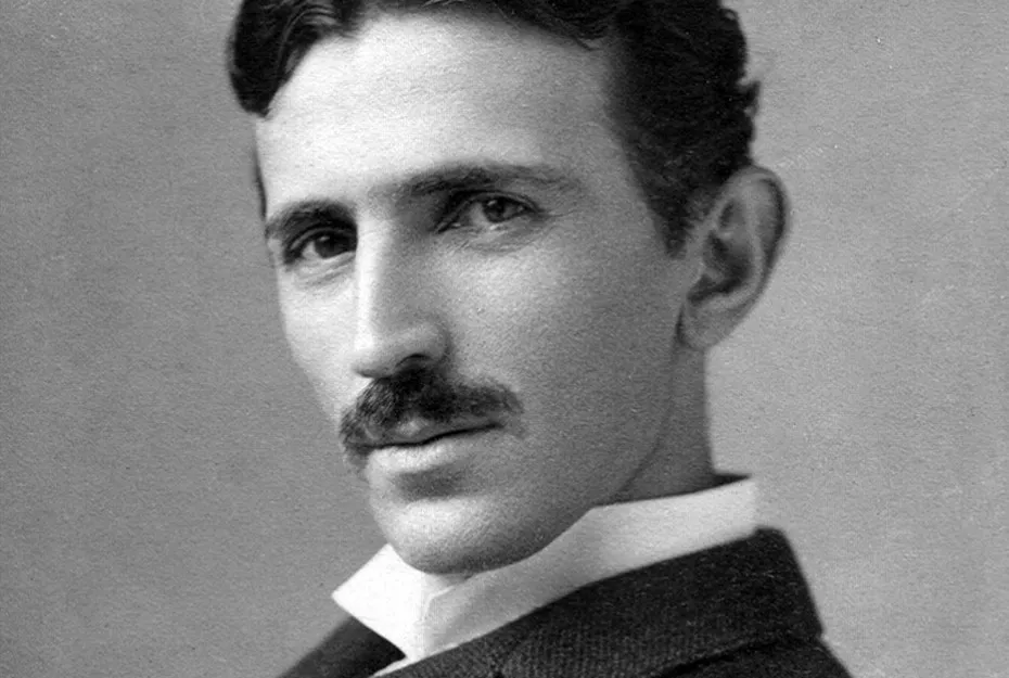 Nikola Tesla in a black and white portrait, wearing a suit and looking thoughtfully toward the camera.