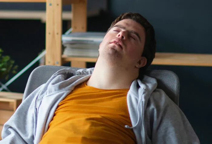 Young man asleep in a chair wearing casual clothes, illustrating exhaustion during weird family traditions or unusual habits.