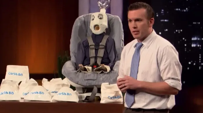 The CarSik Bib was a niche product pitched by Les Cookson on Season 2 of Shark Tank. It was a specialized bib attached around a child’s neck featuring a barf bag designed for young children who suffer from motion sickness in cars but are too young to hold a traditional bag.