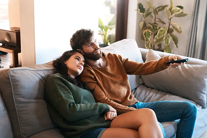 A couple relaxing on a couch together watching TV, portraying men’s thoughts they keep to themselves in relationships.