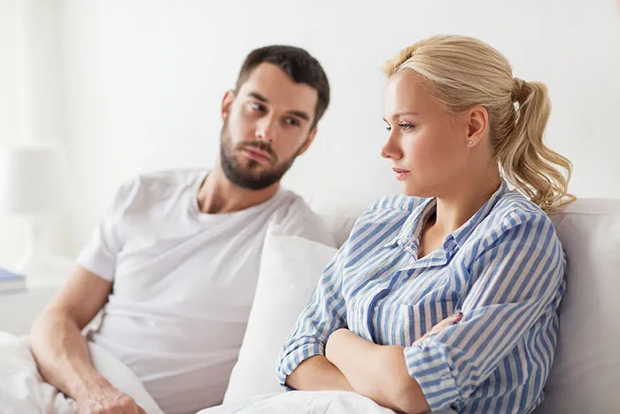 A man and woman sitting on a bed, looking serious, illustrating things men keep to themselves but want to share.