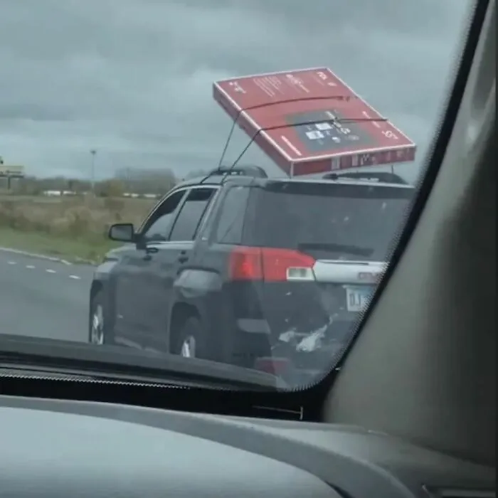 SUV driving with a large TV box improperly tied to the roof, showcasing a funny example of uncultured and ignorant Americans.