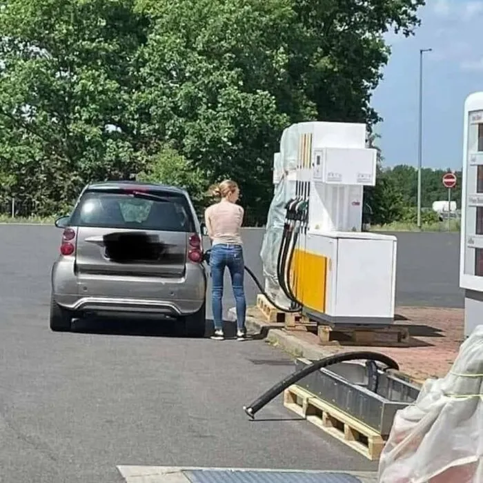 Woman fueling car from wrong side at gas station, highlighting uncultured and ignorant Americans in a humorous way.