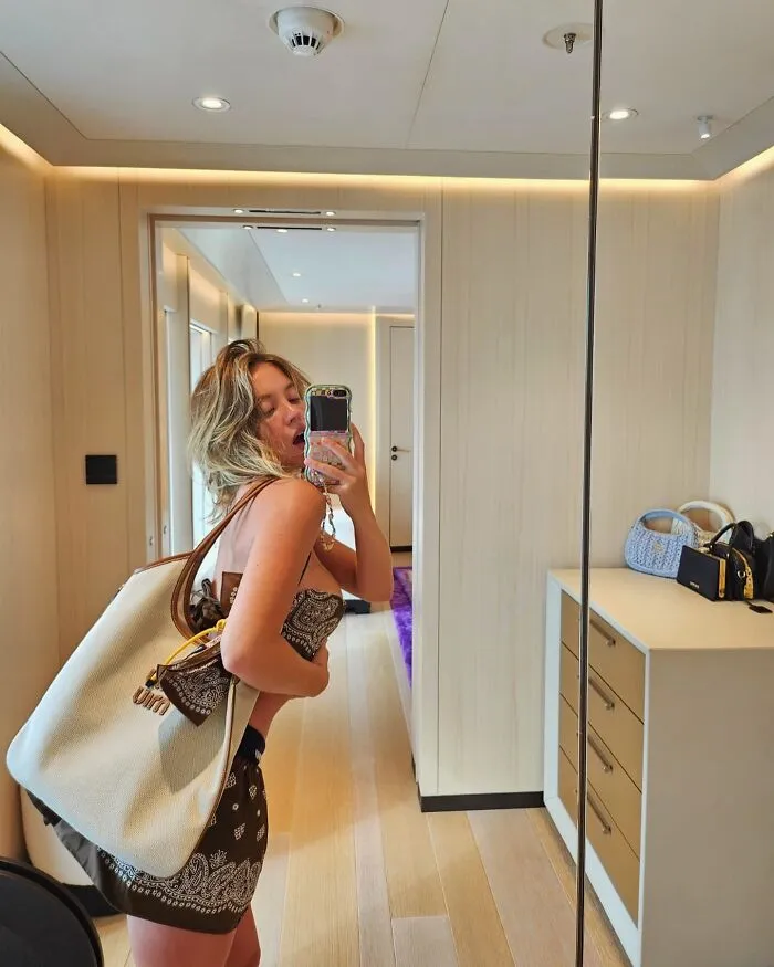 Woman taking a mirror selfie in a modern room, showcasing outfit and large bag, illustrating first dates character-building trauma.