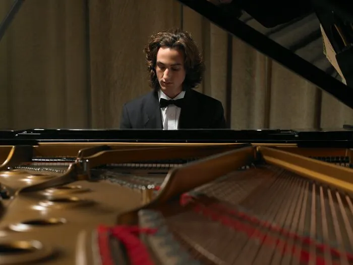 Young man in a tuxedo playing piano, captured from inside the instrument in a dimly lit, eerie setting suggesting haunted places.