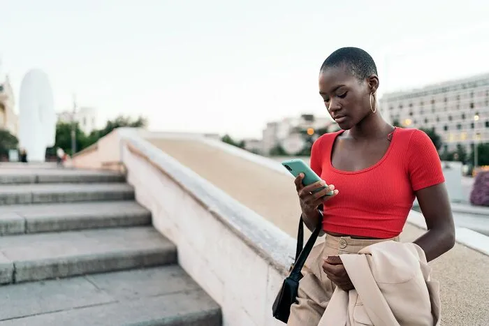 Young woman in a red top holding a phone outdoors, illustrating amazing women shutting down men’s creepy advances.