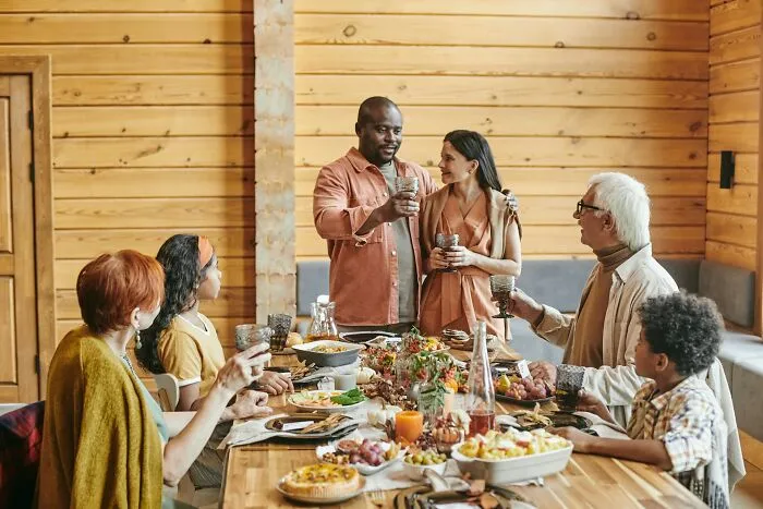 Family celebrating around a wooden table sharing drinks and food, showcasing weird and unhinged family traditions.