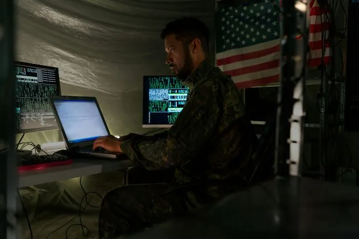 Man in military uniform working on laptop and multiple screens showing data, representing proven facts once stories.