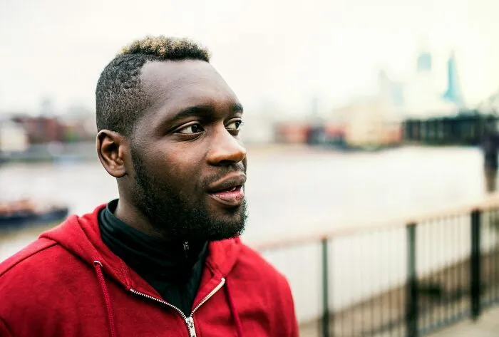 Young man in a red hoodie looking thoughtfully outdoors near a waterfront, illustrating reactions to women shutting down creepy advances.