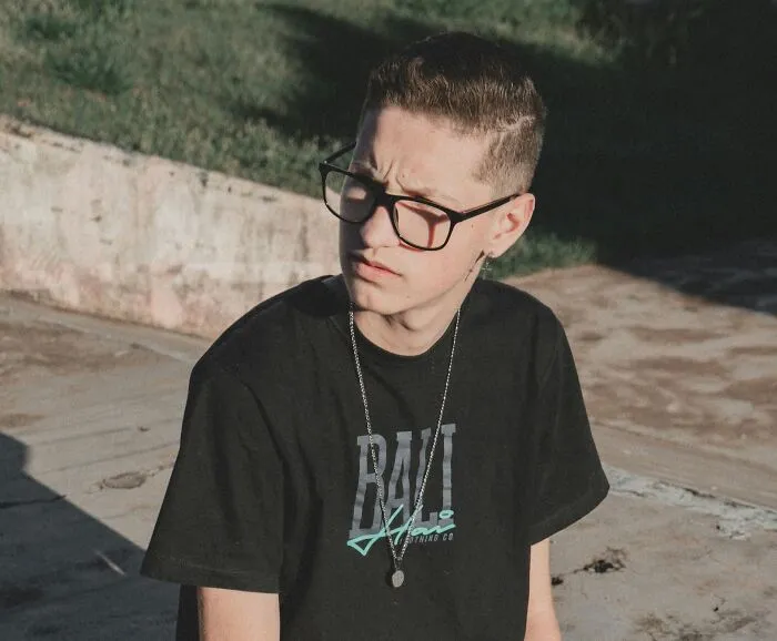 Young man wearing glasses and a black shirt sitting outdoors, reflecting on moments of women shutting down creepy advances.