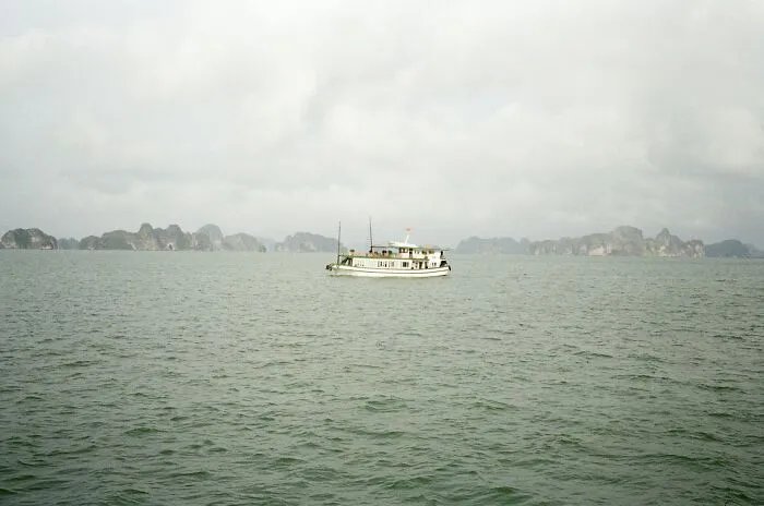 A solitary boat floating on calm sea waters under a cloudy sky with distant rocky islands visible.