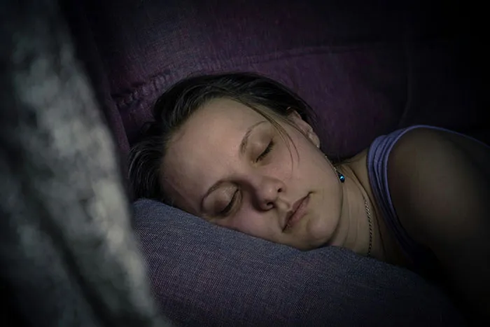 Woman sleeping on a couch at night, illustrating eerie and odd stories about people experiencing unexplained things.