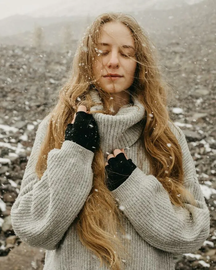 Young woman wearing a gray sweater standing in falling snow, representing well-known facts that are actually fake.