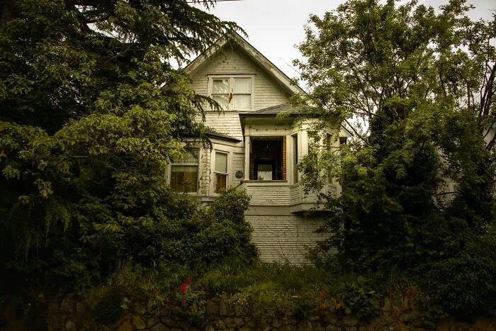 Old abandoned house surrounded by dense trees, evoking spine-chilling haunted place experiences and eerie basement vibes.