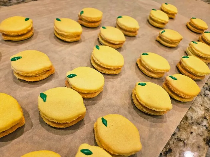 Yellow lemon-shaped macarons with green decoration on baking tray