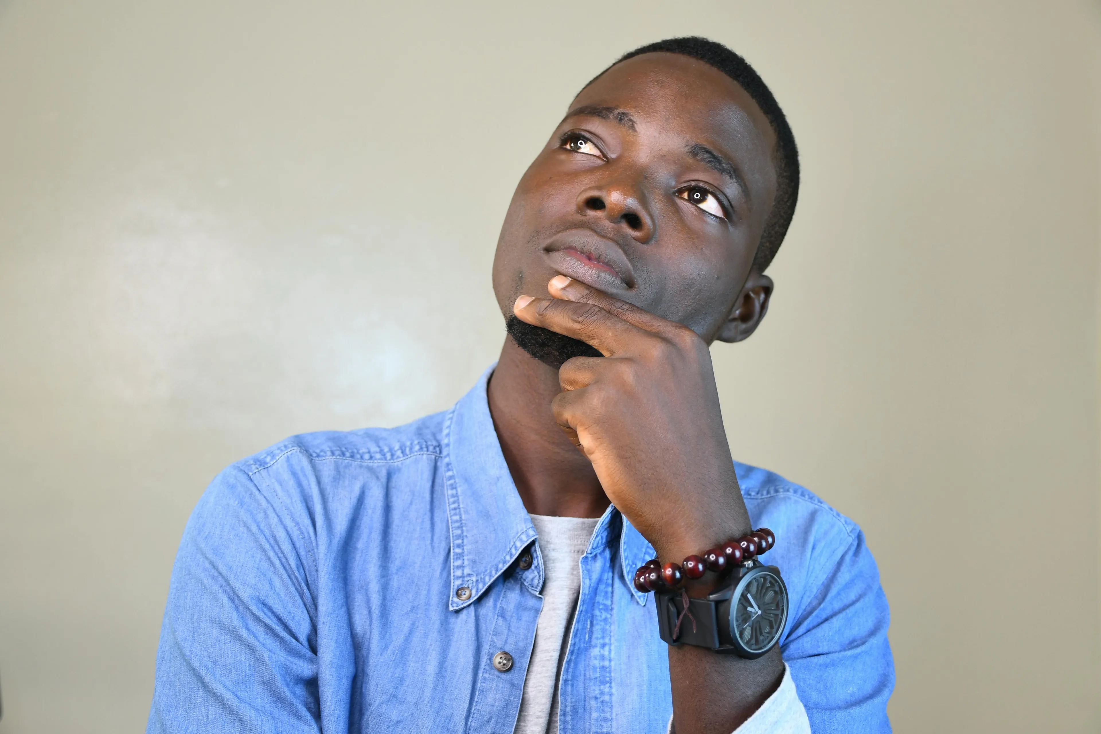 Young man in a blue shirt thoughtfully looking up, representing courage meter while staying somewhere unfamiliar.