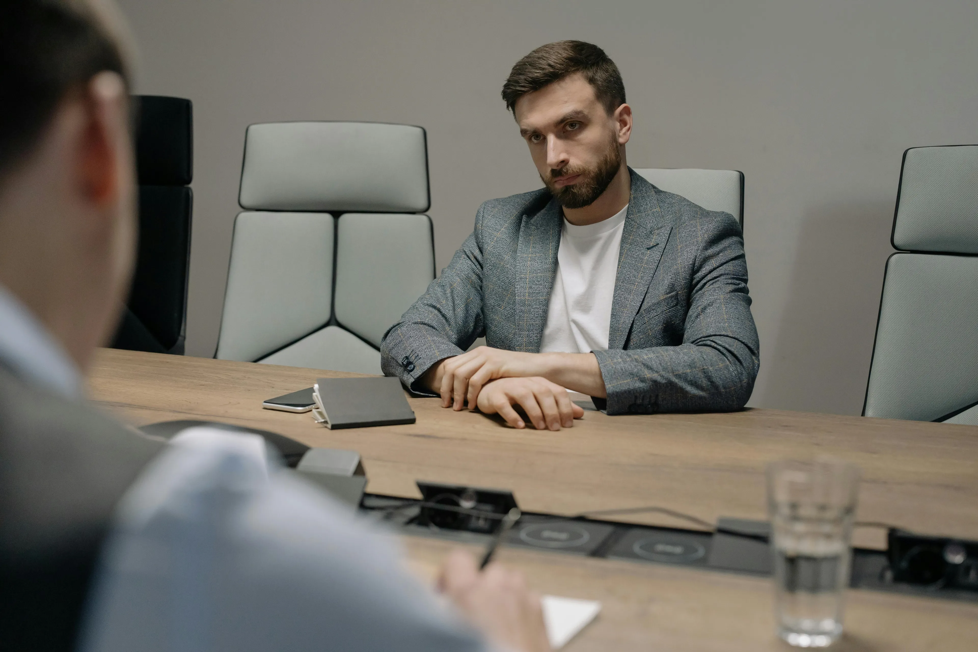 Man in a gray blazer sitting at a conference table showing courage meter while preparing to ask boss for a raise.