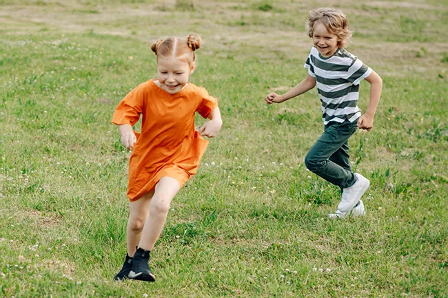 Two children playing and running on grass, enjoying a classic childhood game brought back for adults.