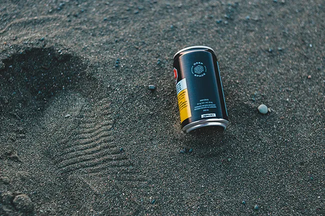 Empty soda can lying on sandy ground near footprints, evoking memories of outdoor kick the can games for adults.