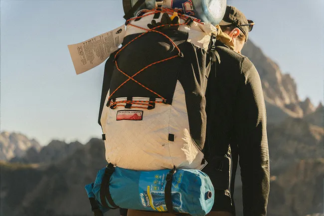 Backpacker with large backpack and gear, hiking outdoors with no itinerary in mountainous terrain under clear sky