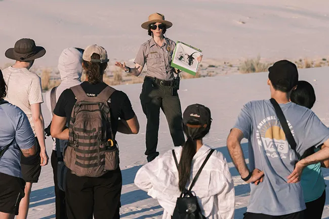 Park ranger leading a guided group tour in a desert setting, engaging a diverse group of travelers outdoors.